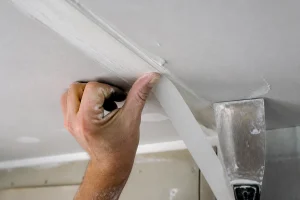 Pose d'une bande à joint en papier sur un enduit placo à l'aide d'un couteau à enduire