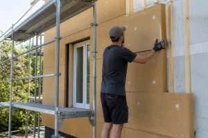 Particulier posant des panneaux isolants sur une façade lors d'une isolation extérieure soi-même